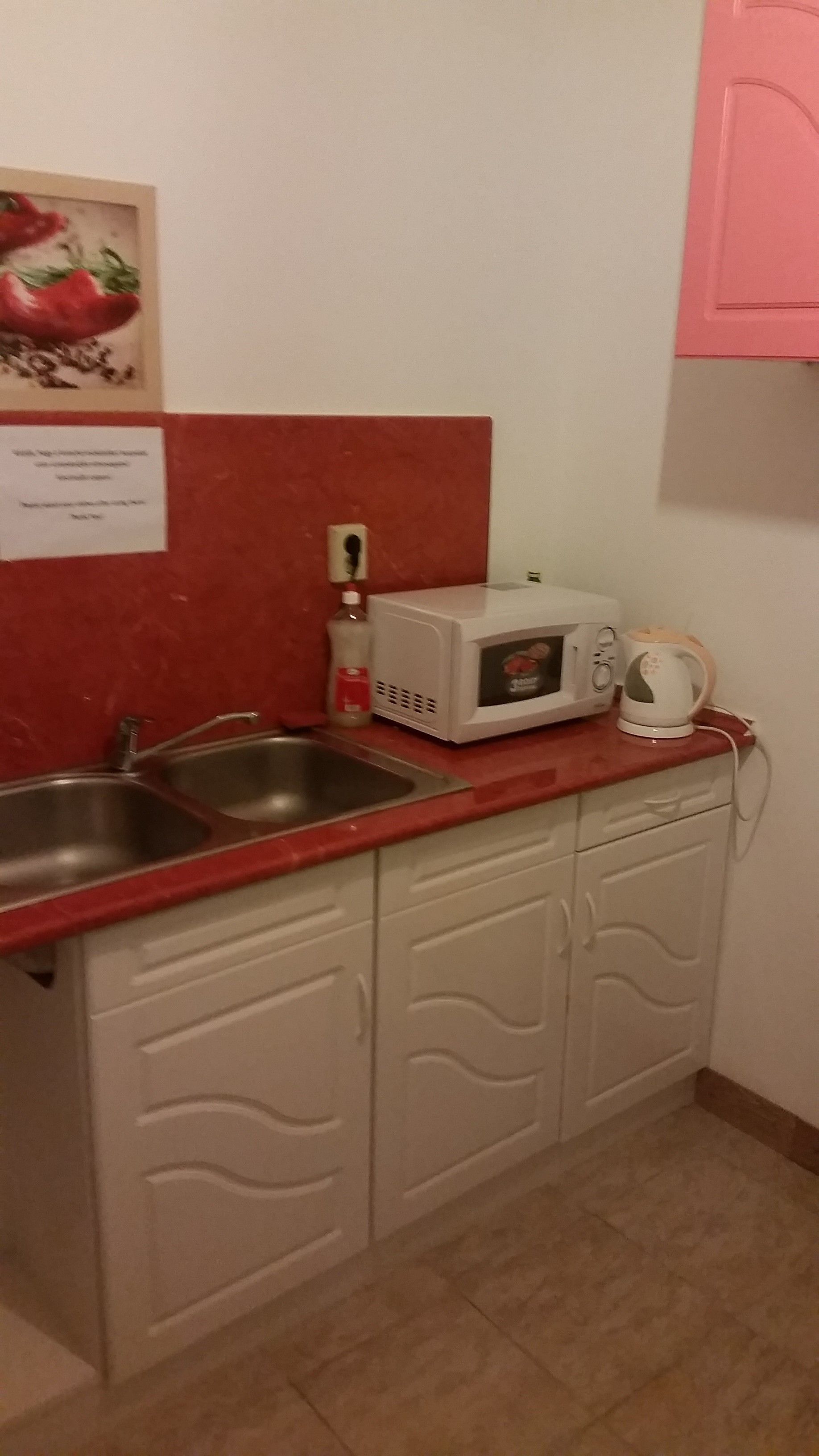 A kitchen with a red countertop, a white microwave, a kettle, and a sink.