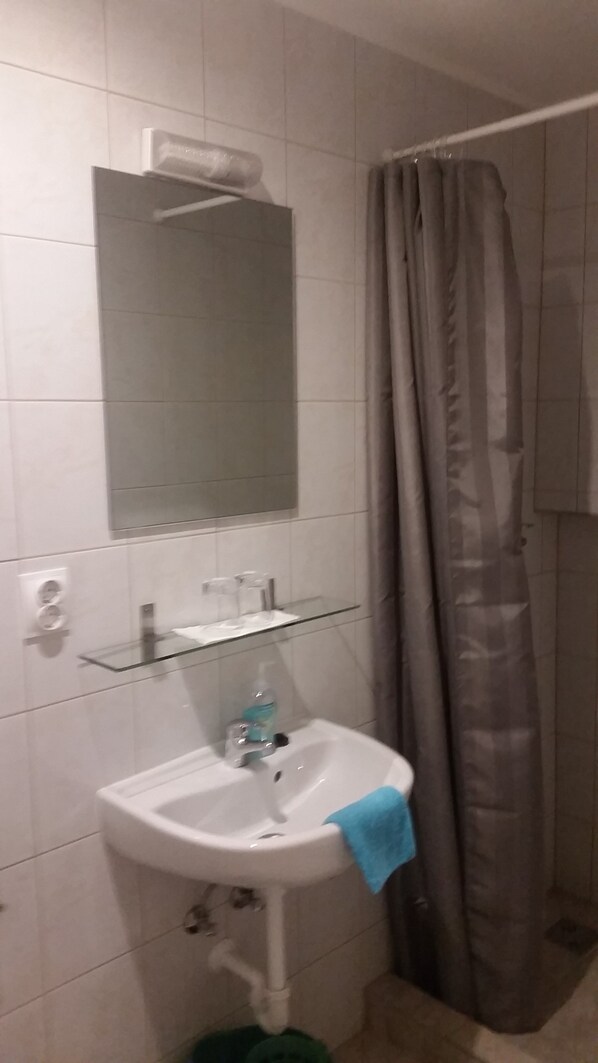 A bathroom with a white sink, a glass shelf above it, a mirror, and a shower curtain.