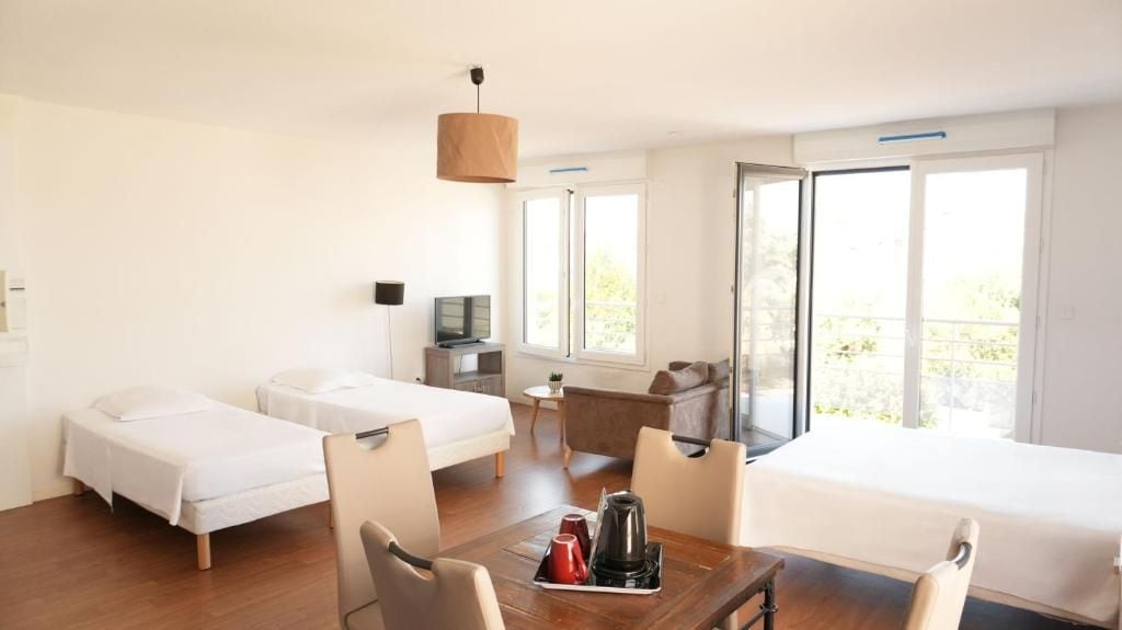 A hotel room with two beds, a desk, a chair, a table with a kettle, and a TV.