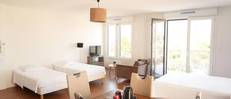 A hotel room with two beds, a desk, a chair, a table with a kettle, and a TV.