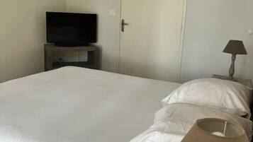 Ein Schlafzimmer mit einem Bett, einem Fernseher auf einem Schrank, einer Tür und einer Lampe auf einem Nachttisch.