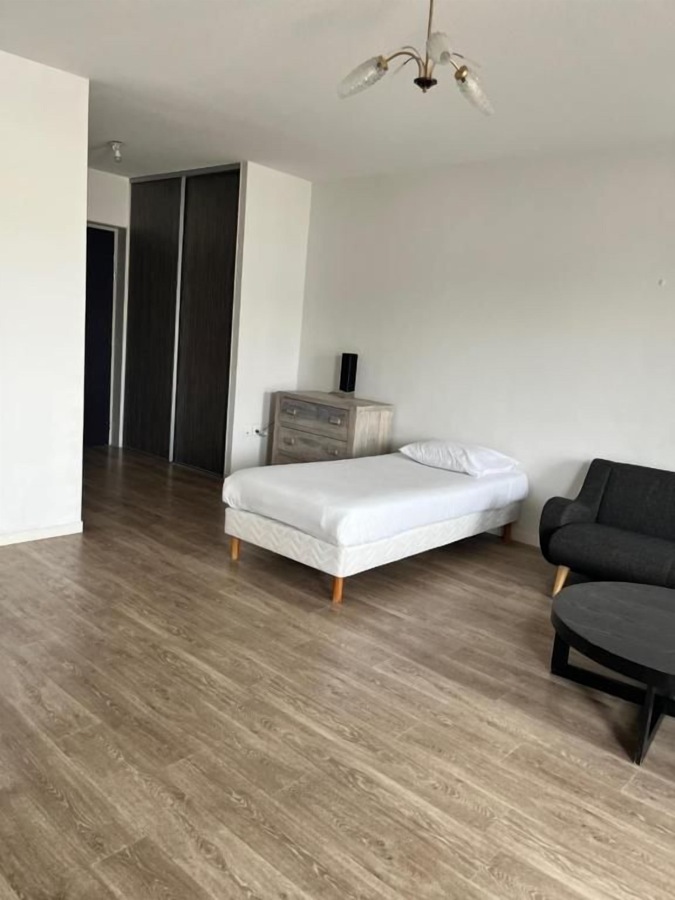 A bedroom with a bed, a dresser, a black sofa, and a wooden floor.