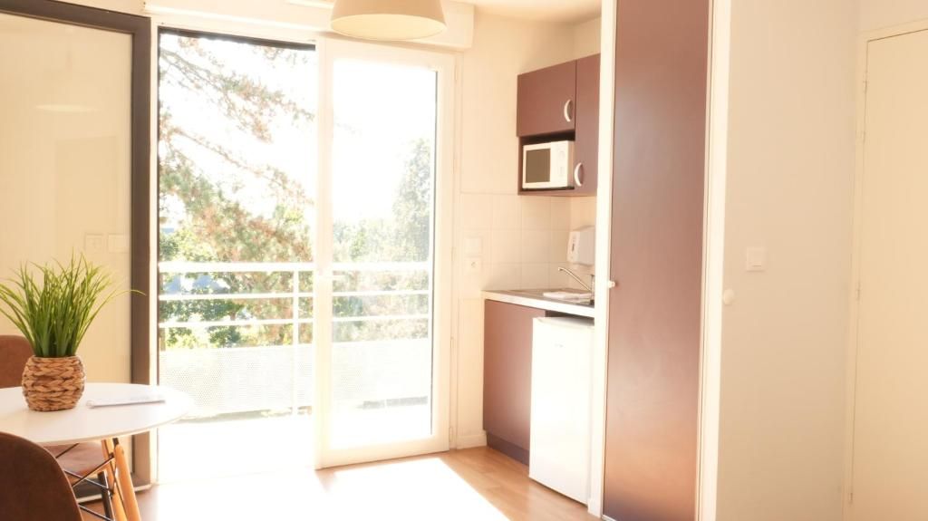 Una cocina compacta con microondas, un lavamanos pequeño y una puerta corrediza de vidrio que da a un balcón.