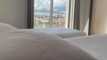 Ein Hotelzimmer mit zwei Betten, einem großen Fenster und Blick auf die Stadt.