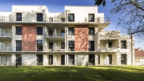 Un edificio residencial de varios pisos con balcones, techo plano y césped bien cuidado.