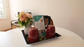 Une table blanche avec une brochure, un vase de fleurs et deux tasses rouges.