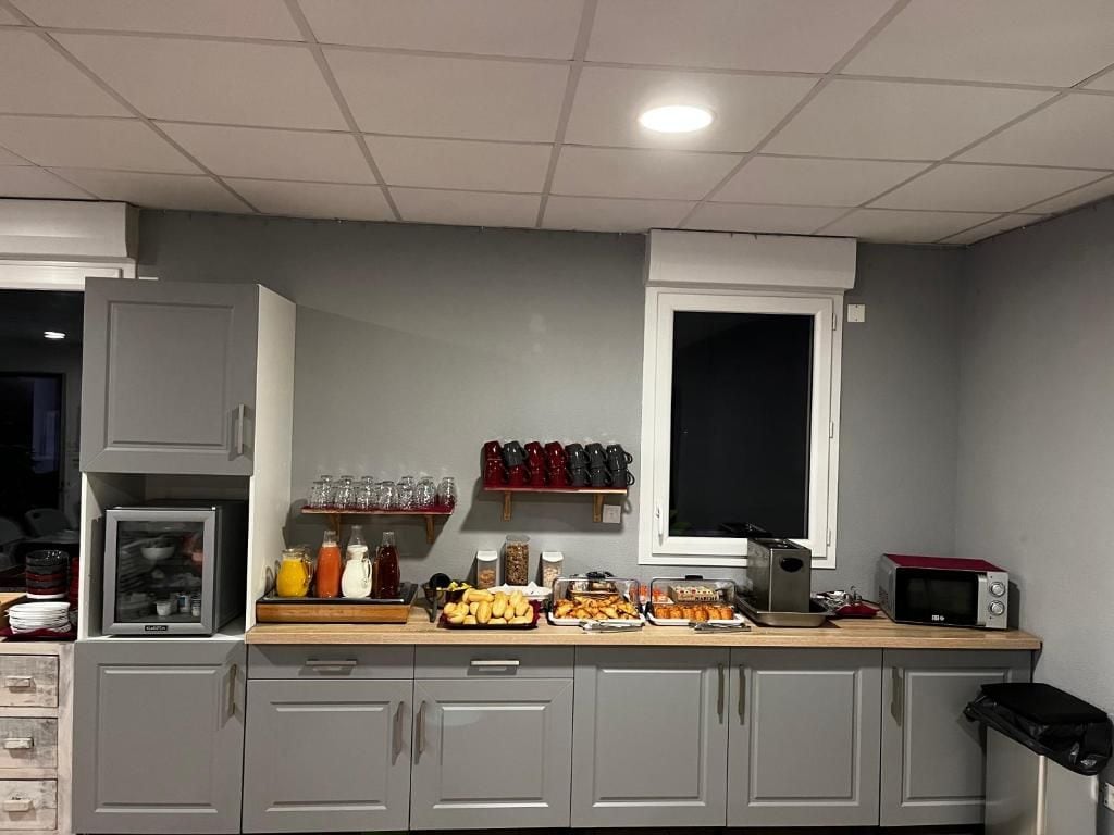 A kitchen with grey cabinets, a microwave, and a variety of food items on the counter.