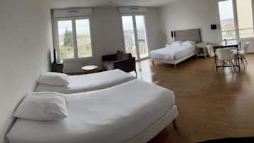 A hotel room with two beds, a dining table with chairs, a small round table, and a view through the window.
