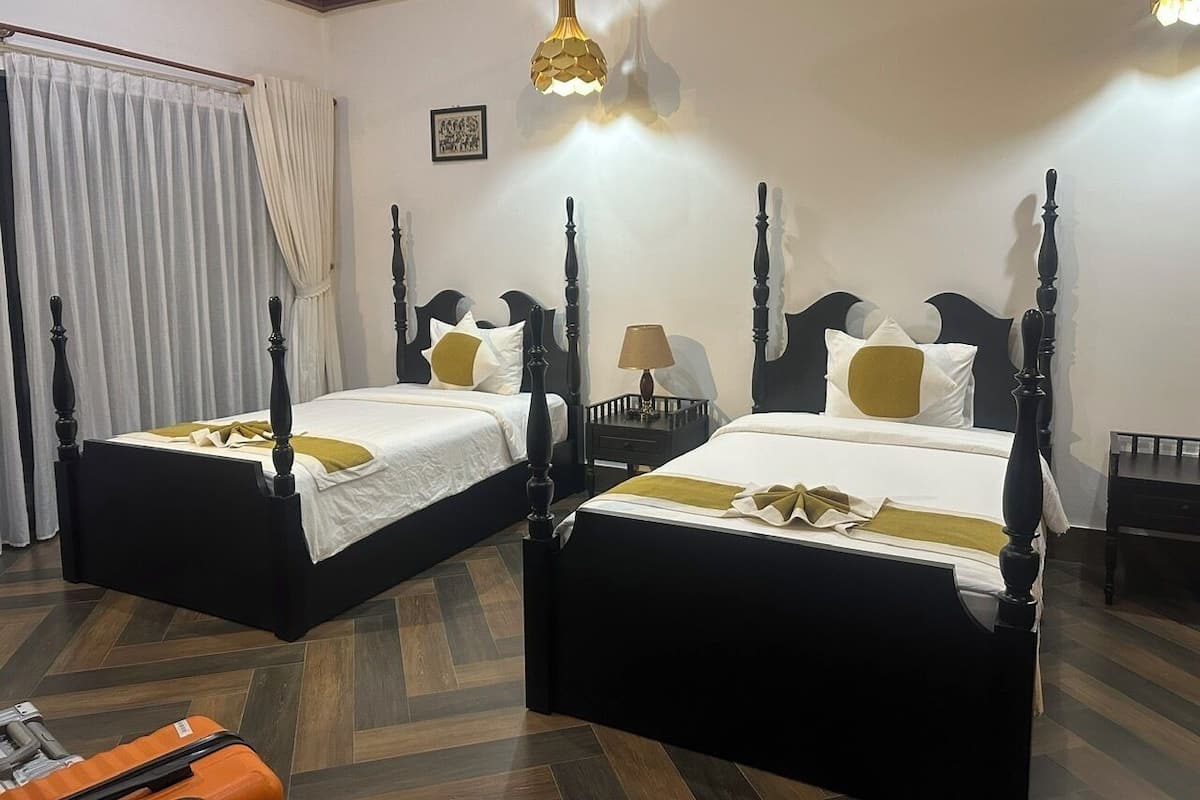 Een hotelkamer met twee zwarte hemelbedden, witte beddengoed en een houten vloer.