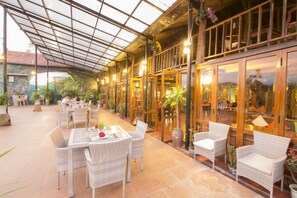 An indoor/outdoor dining area with wicker furniture, glass doors, and potted plants.
