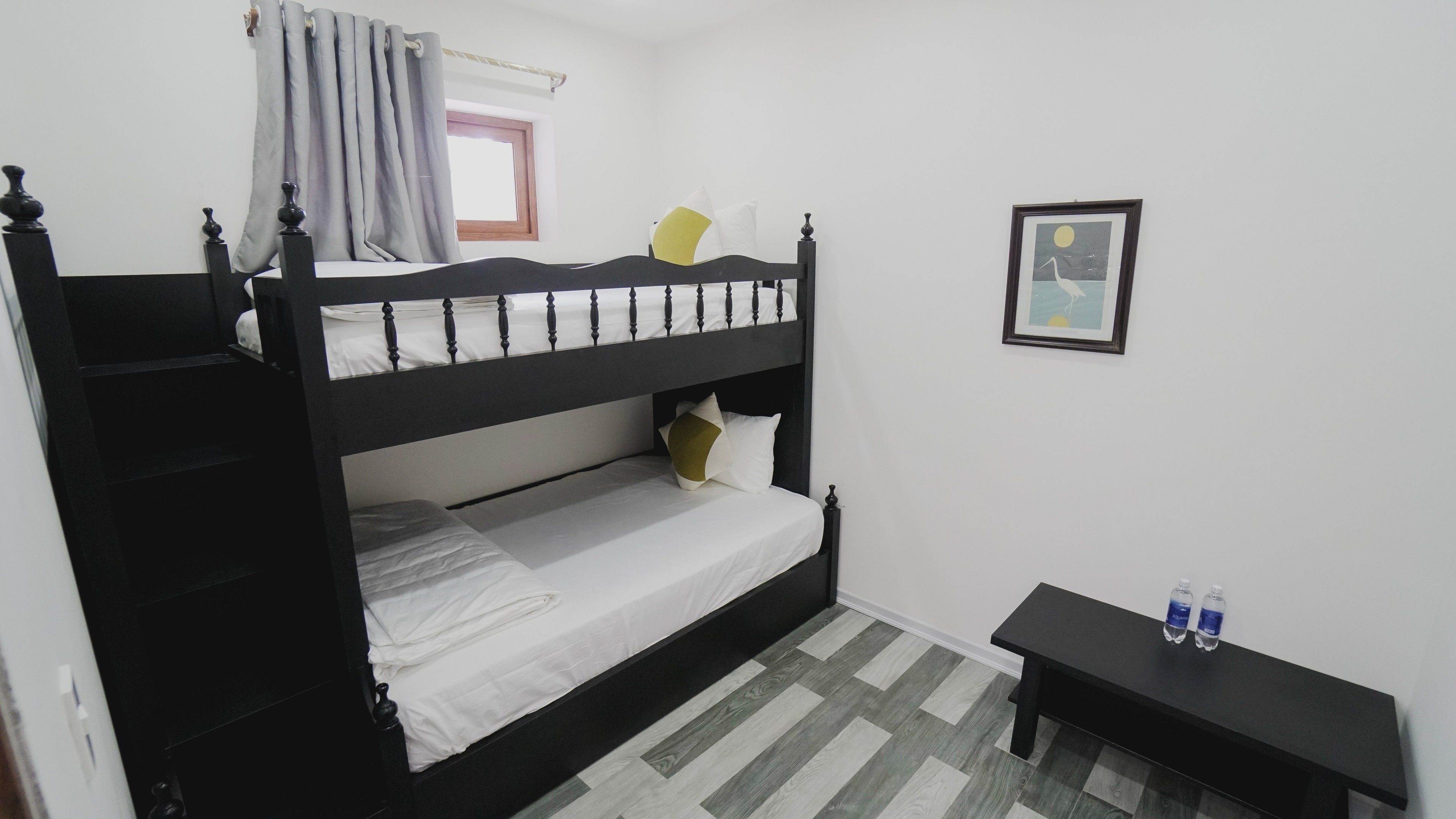 Habitación con literas, una ventana, un cuadro en la pared y una mesita con botellas de agua.