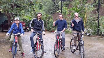Four people on bicycles in an outdoor setting with greenery and a dirt path.