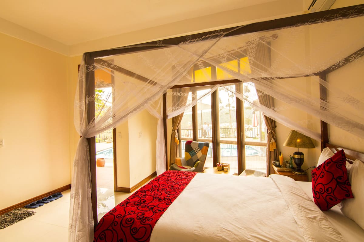 Een slaapkamer met een hemelbed, een rood tapijt en uitzicht op buiten.