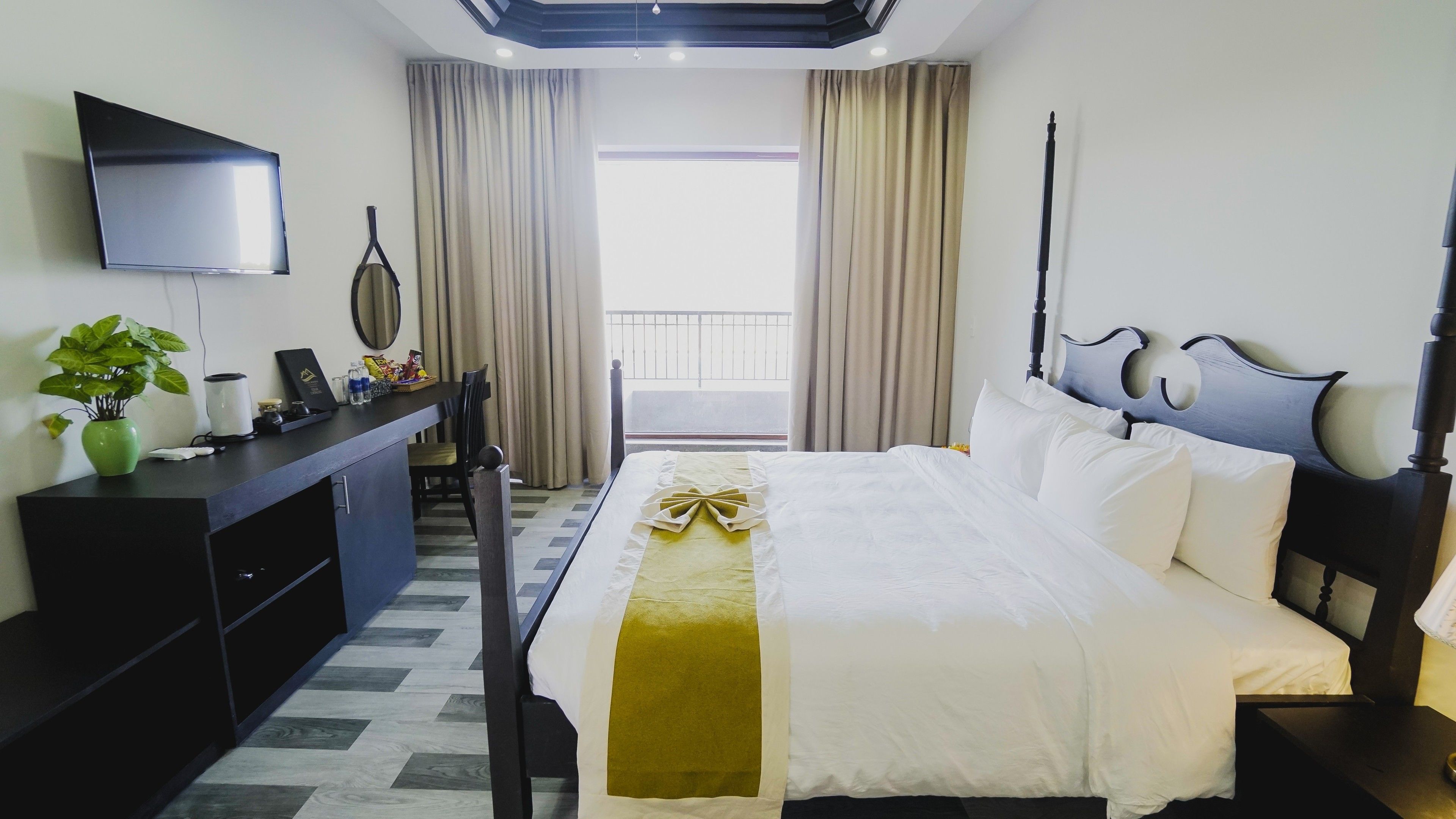 A hotel room with a bed, a desk, a chair, a TV, and a balcony with curtains.