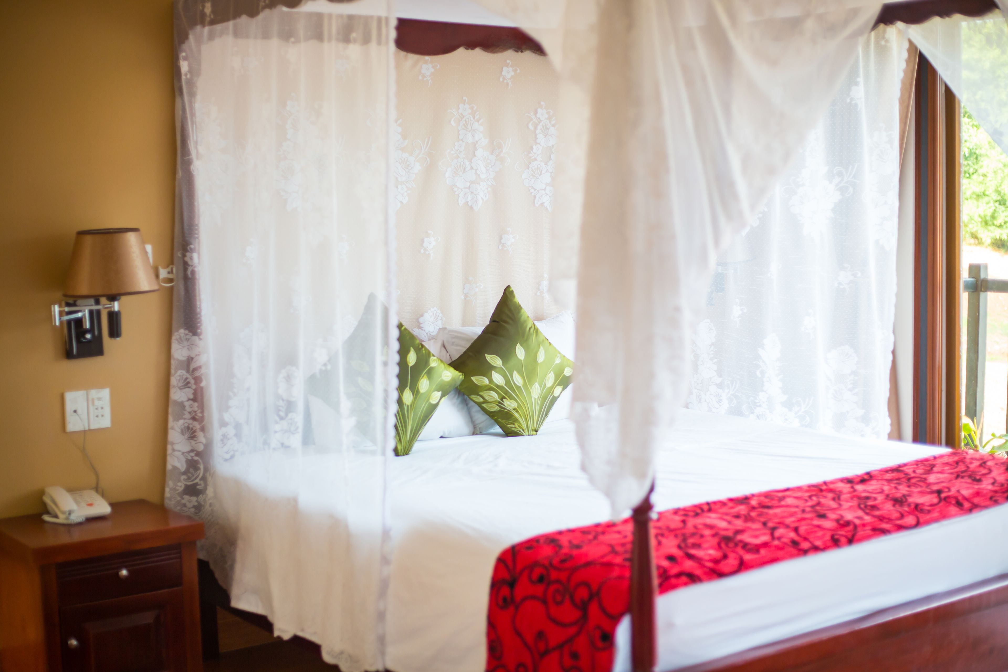 A bedroom with a canopy bed, a bedside table with a lamp, and a telephone.