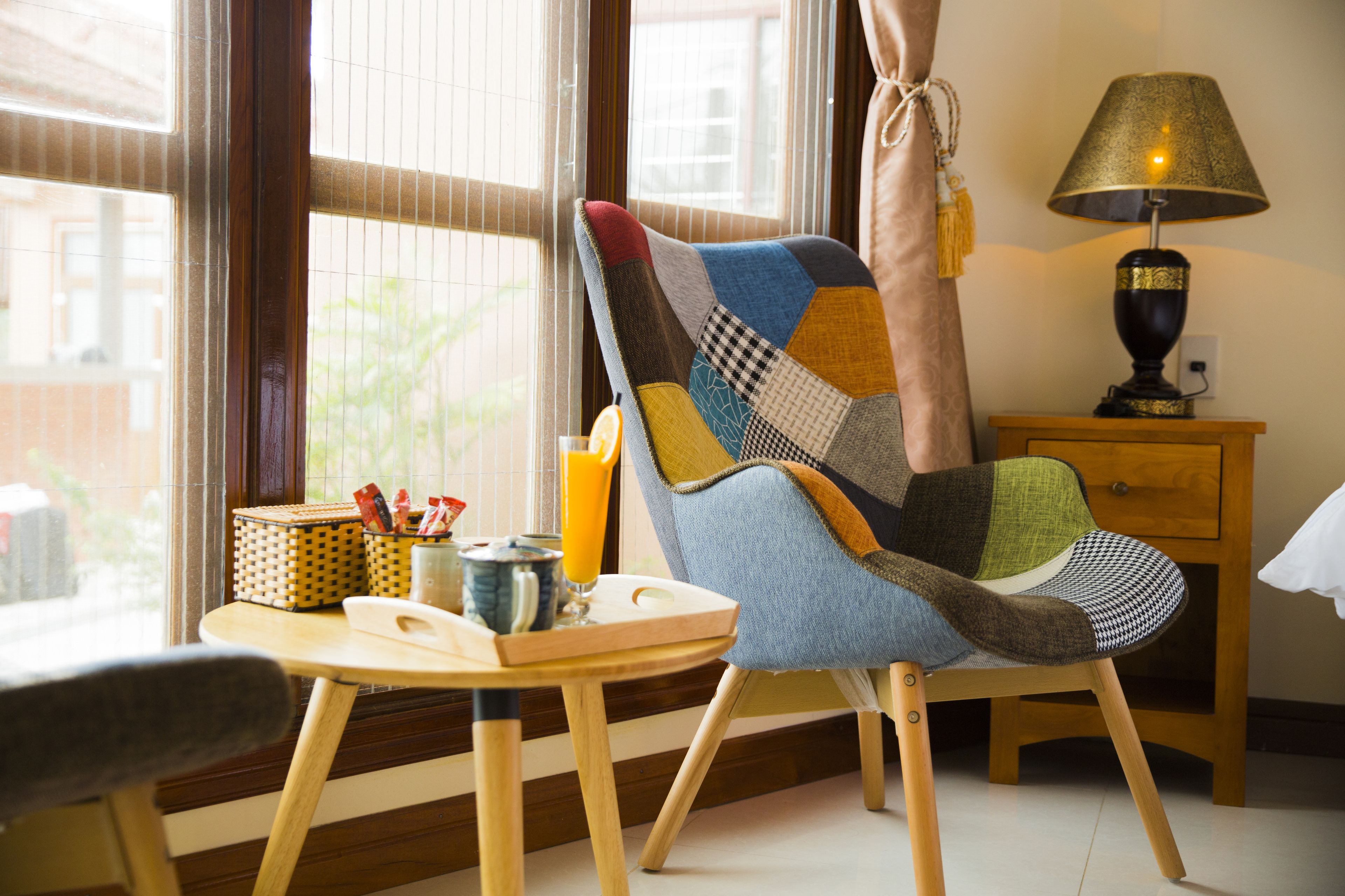 A cozy room with a wooden chair, a small table with a glass of orange juice, and a lamp on a wooden nightstand.