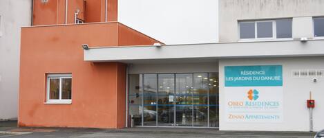 Un edificio con una amplia entrada de vidrio, un letrero que indica OBEO Residences y un estacionamiento al frente.
