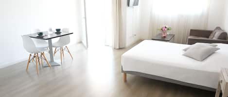 Una habitación de hotel moderna con cama, escritorio y sillas, una pequeña mesa con un jarrón y un sofá.