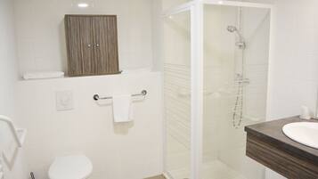Un baño moderno con inodoro, ducha de vidrio, mueble de madera y lavamanos.