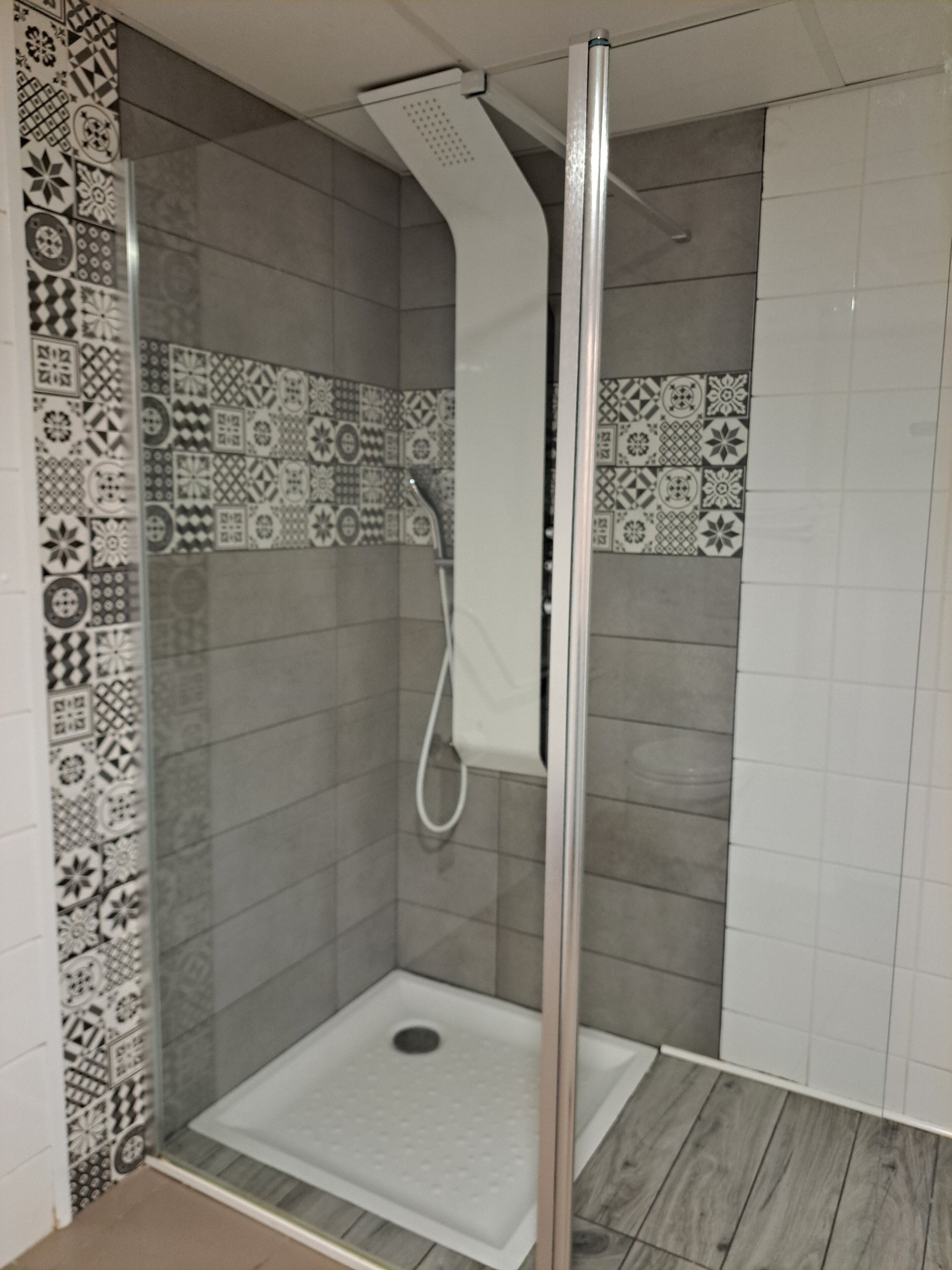 Een douche met een glazen deur, betegelde wanden en een witte douchekop.