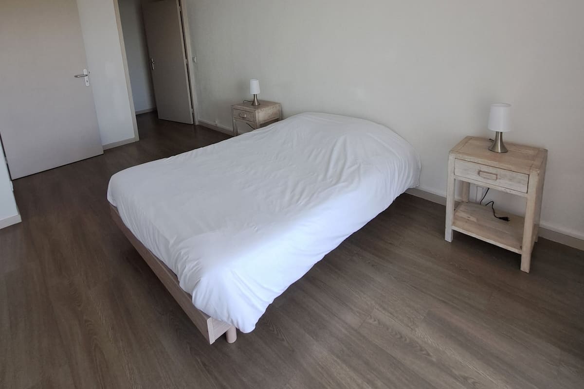 Un dormitorio con cama, mesita de noche con lámpara, suelo de madera y lámpara en el techo.