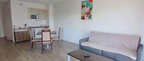 Una sala de estar moderna con un sofá gris, una mesa de centro y un comedor con una silla y un microondas.