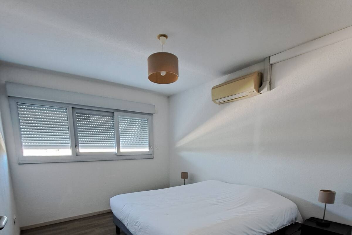 Un dormitorio con cama, ventana con persianas, ventilador de techo y aire acondicionado.