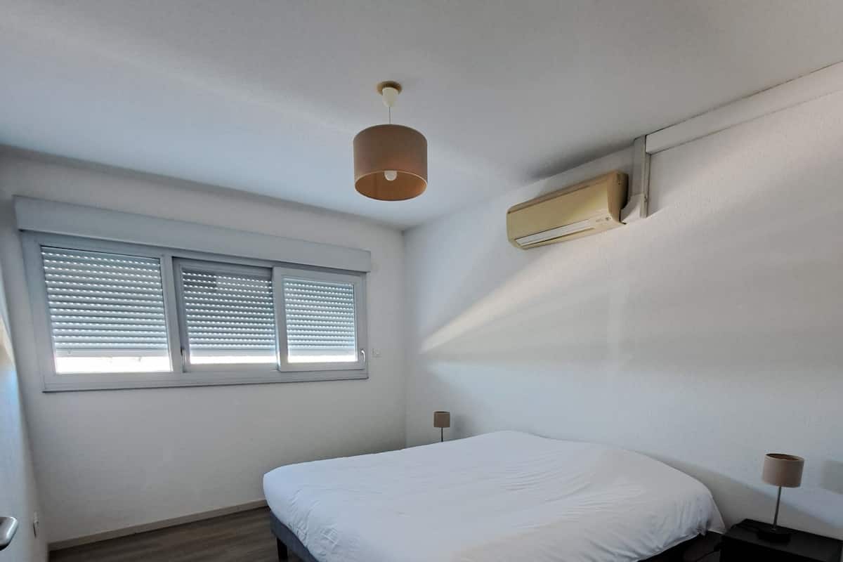 A bedroom with a bed, a window with blinds, a ceiling fan, and an air conditioning unit.