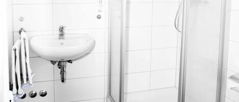 Un baño moderno con ducha de vidrio, lavamanos blanco y suelo de baldosas.