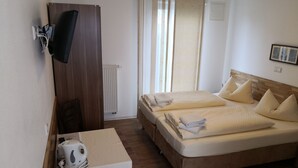 Ein Hotelzimmer mit zwei Betten, einem Schreibtisch mit Wasserkocher, einem an der Wand befestigten Fernseher und einem Fenster mit Vorhängen.