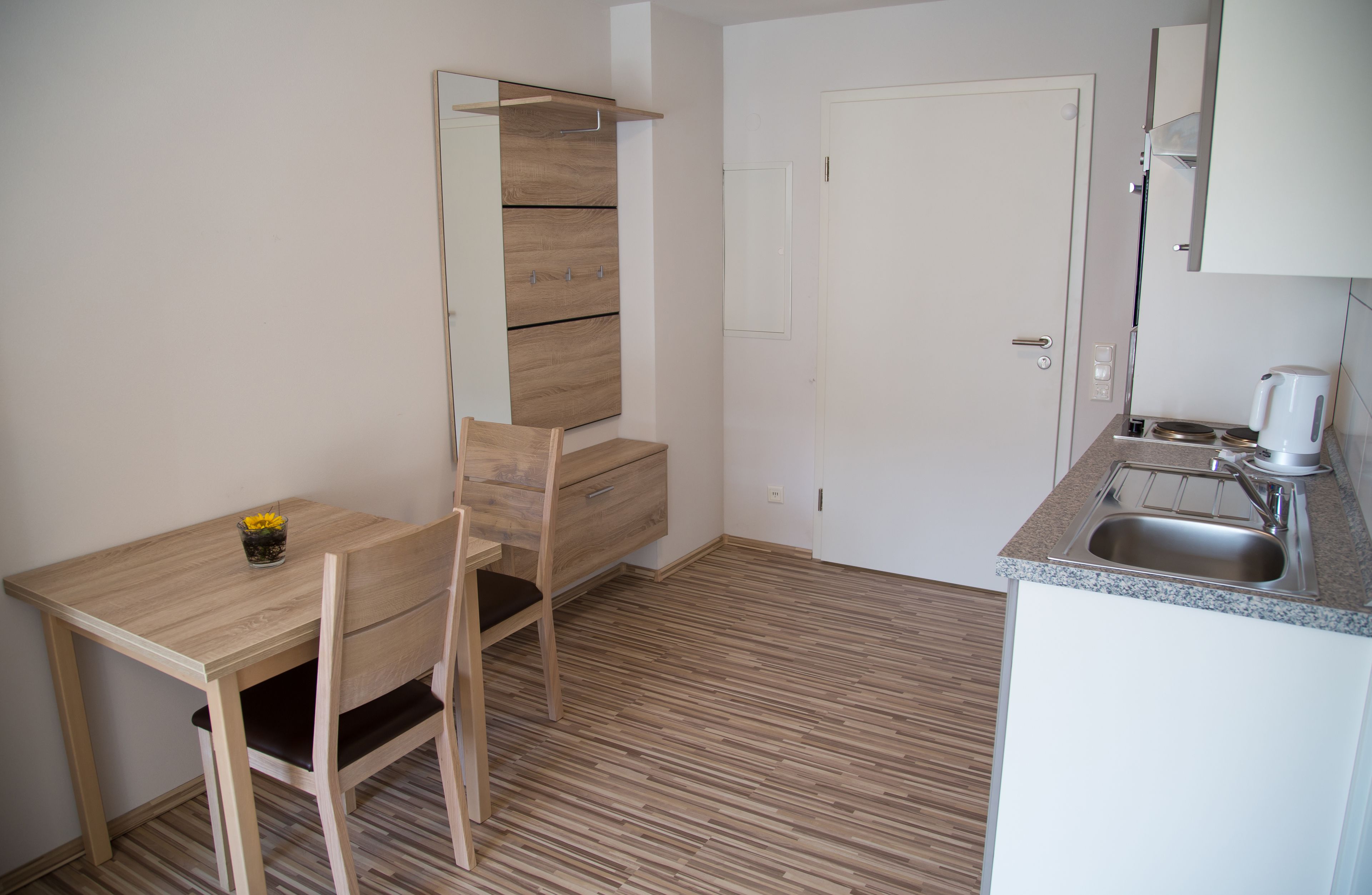 Una cocina compacta con una mesa de madera, una silla, un mueble pequeño y un lavamanos.