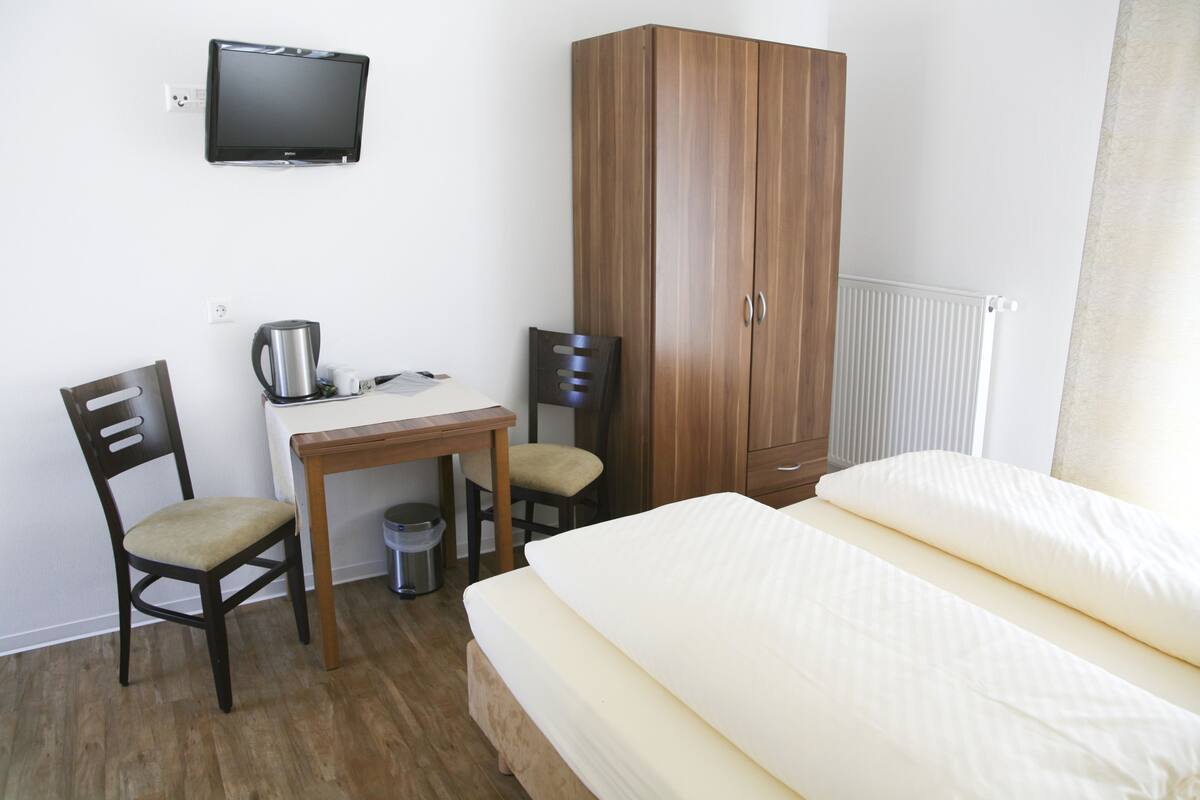 Ein Hotelzimmer mit einem Bett, einem Schreibtisch mit Stuhl, einem Fernseher und einem Kleiderschrank.