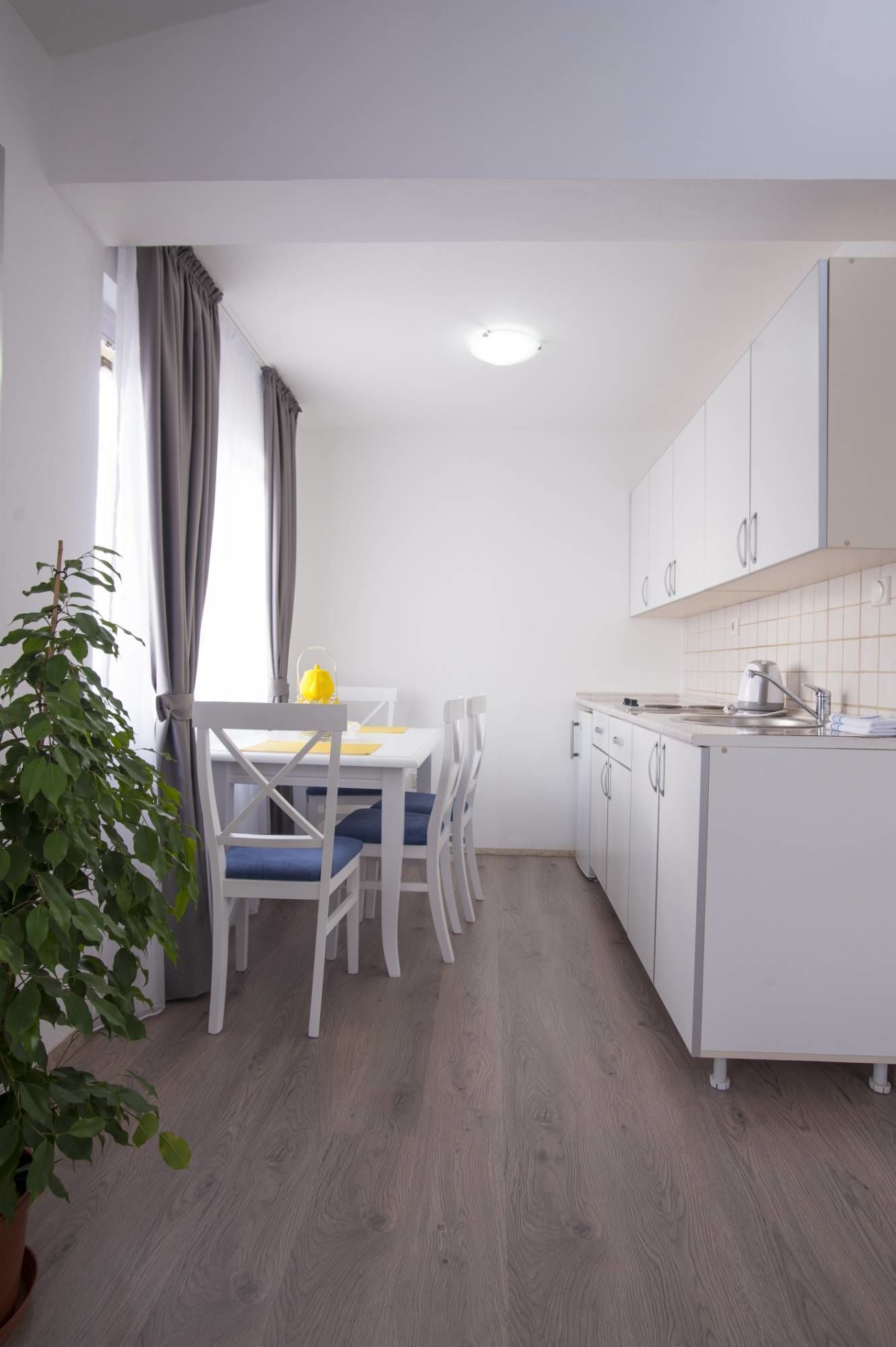 Cozinha moderna com armários brancos, área de refeições com mesa e cadeiras, e um vaso de planta.