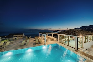 A swimming pool with lounge chairs and a covered seating area, overlooking a body of water.