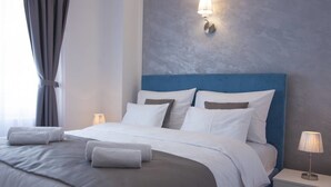 Una habitación de hotel moderna con una cama bien tendida, una mesita de noche con lámpara y un ventanal con cortinas.