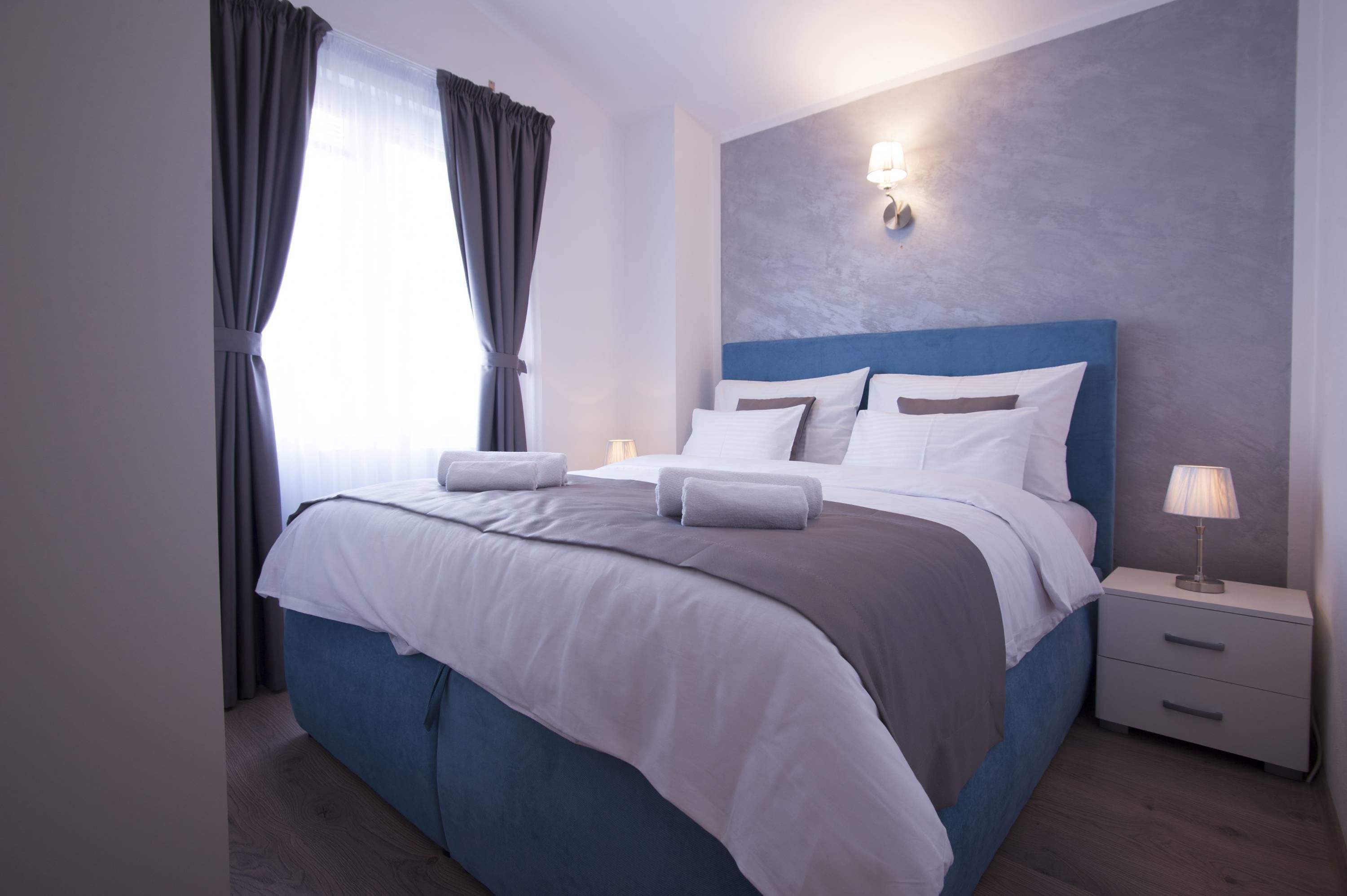 A modern bedroom with a large bed, a nightstand, and a wall-mounted lamp.