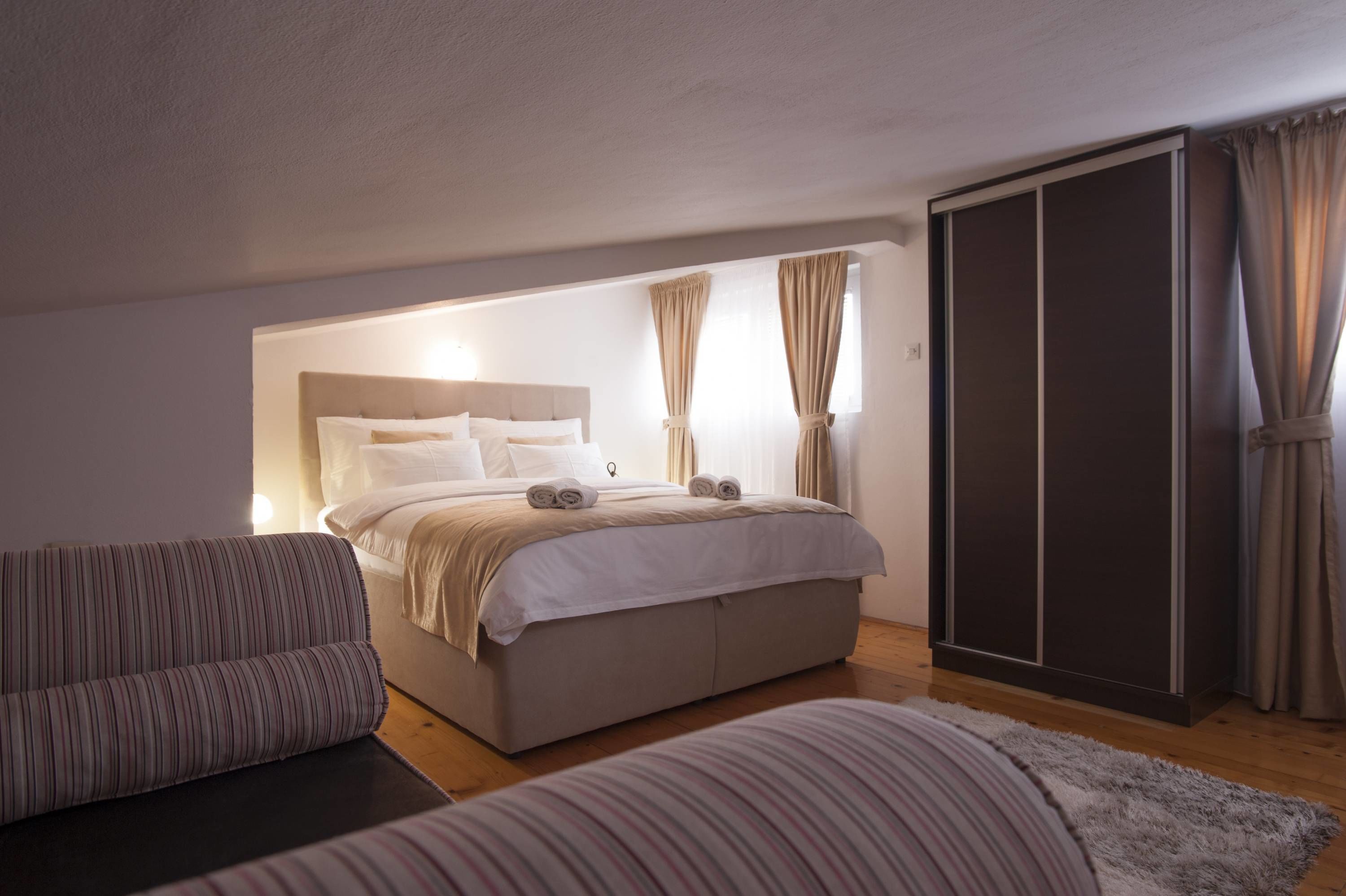 A bedroom with a bed, a sofa, a wardrobe, and curtains.
