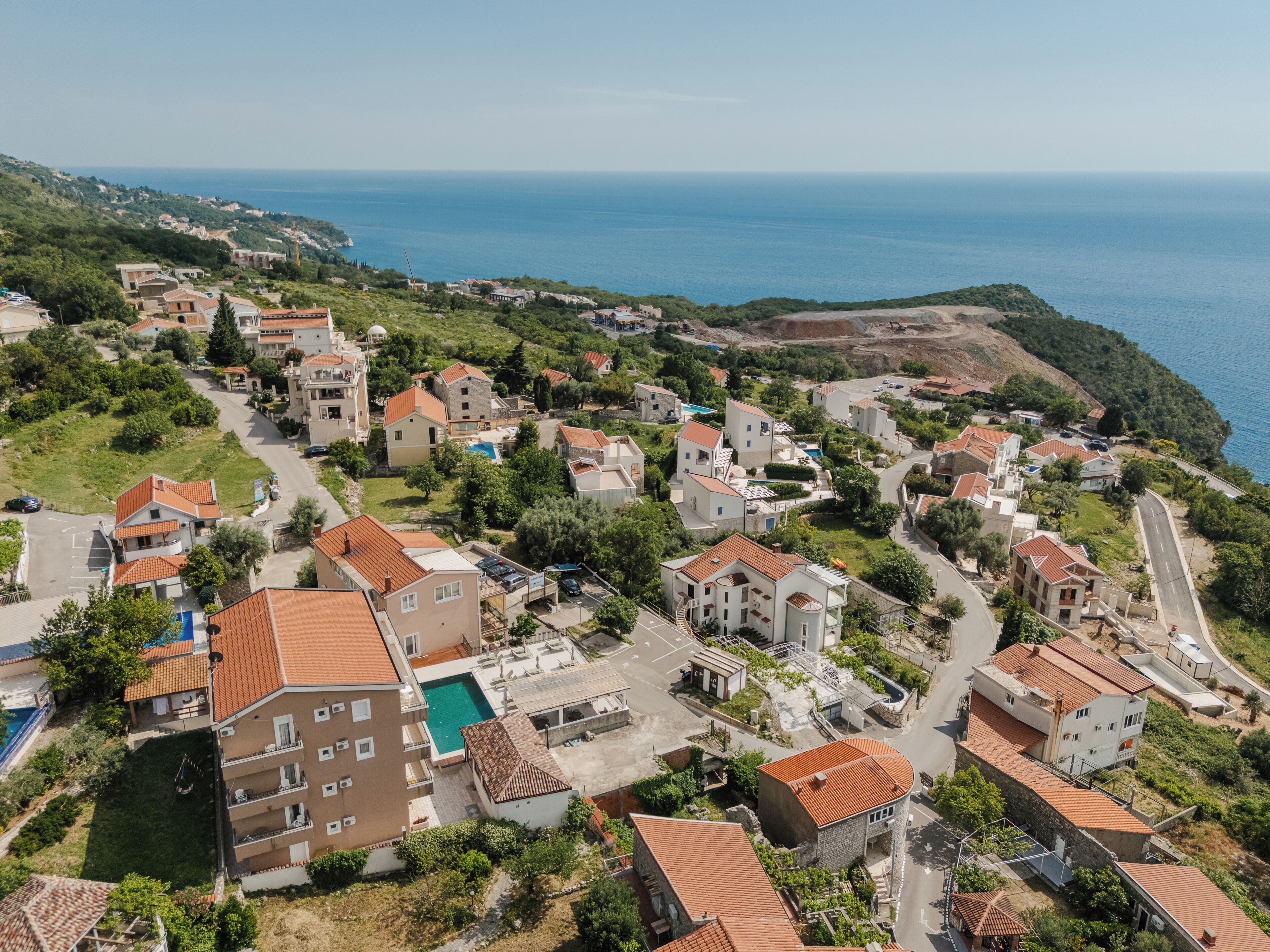A coastal residential area with houses, a swimming pool, and a view of the sea.