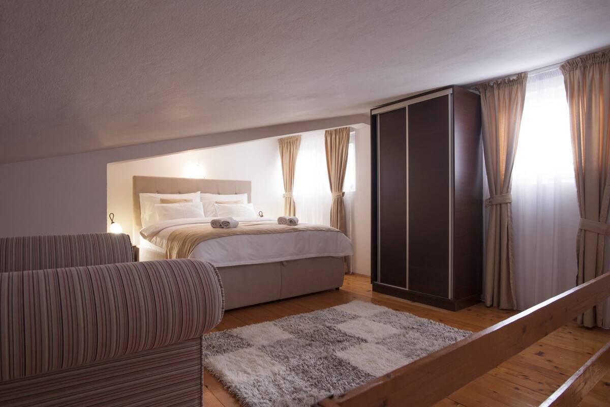 A bedroom with a bed, a sofa, a wardrobe, and a staircase.
