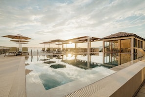 A pool area with lounge chairs and umbrellas, a glass-enclosed building, and a clear sky.