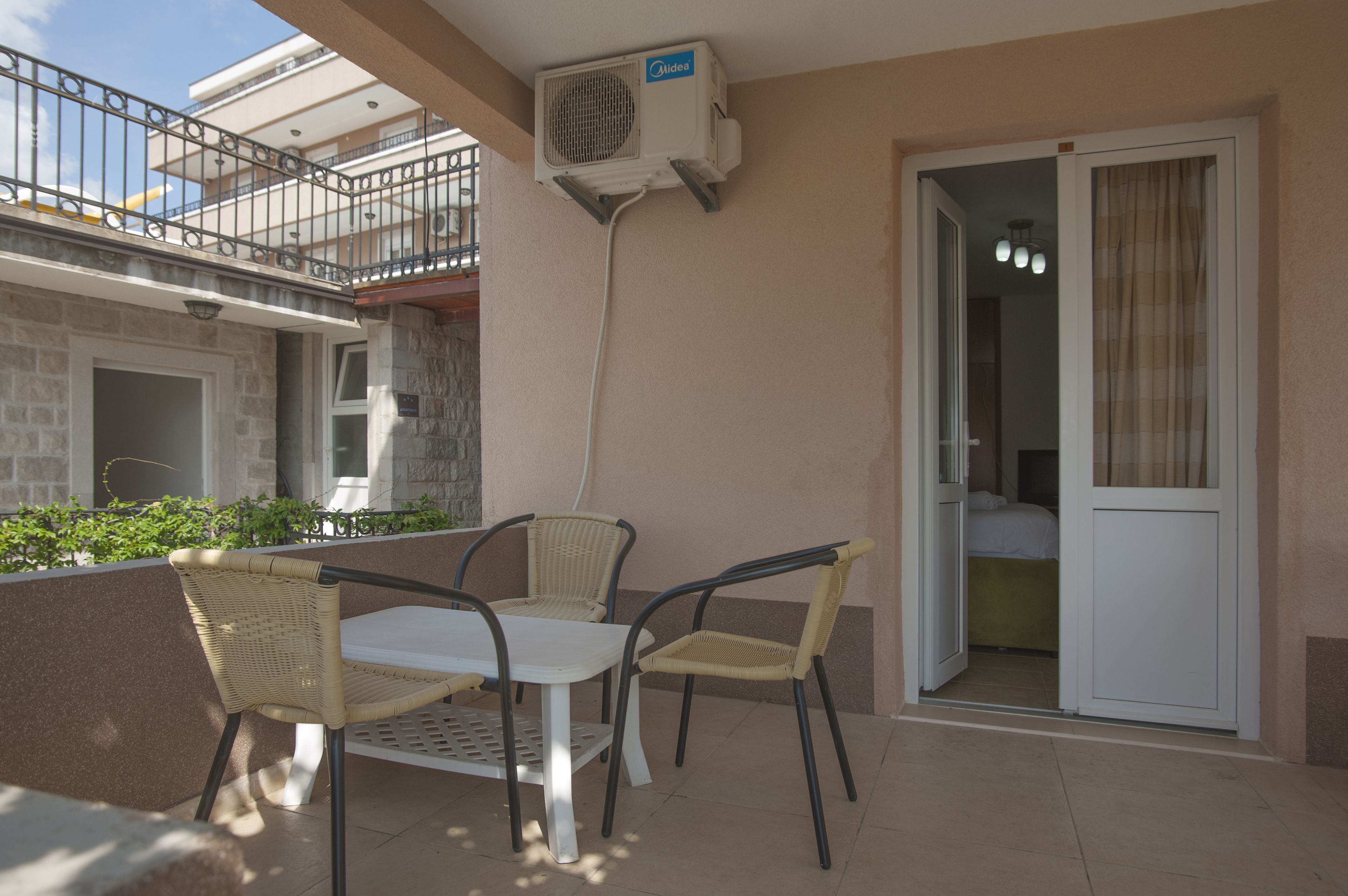 An outdoor balcony with a table and chairs, an air conditioning unit, and a sliding glass door leading to a bedroom.