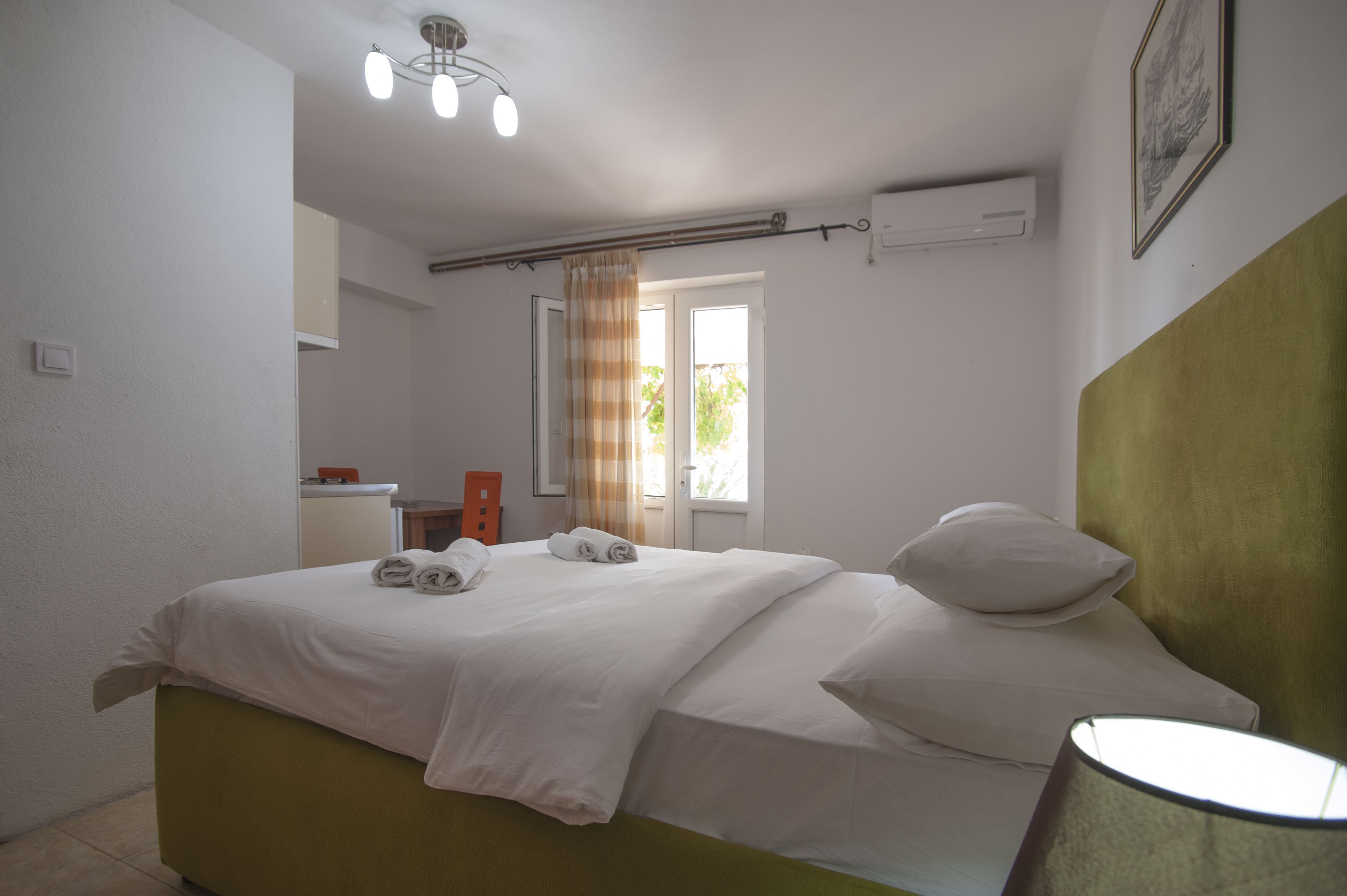 A hotel room with a bed, a bedside lamp, a window with curtains, and a ceiling light fixture.