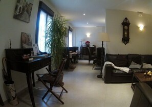 A living room with a dark brown leather sofa, a wooden coffee table, a dining table with chairs, a potted plant, and a wall-mounted clock. - Casa del Castillo (Siguenza)
