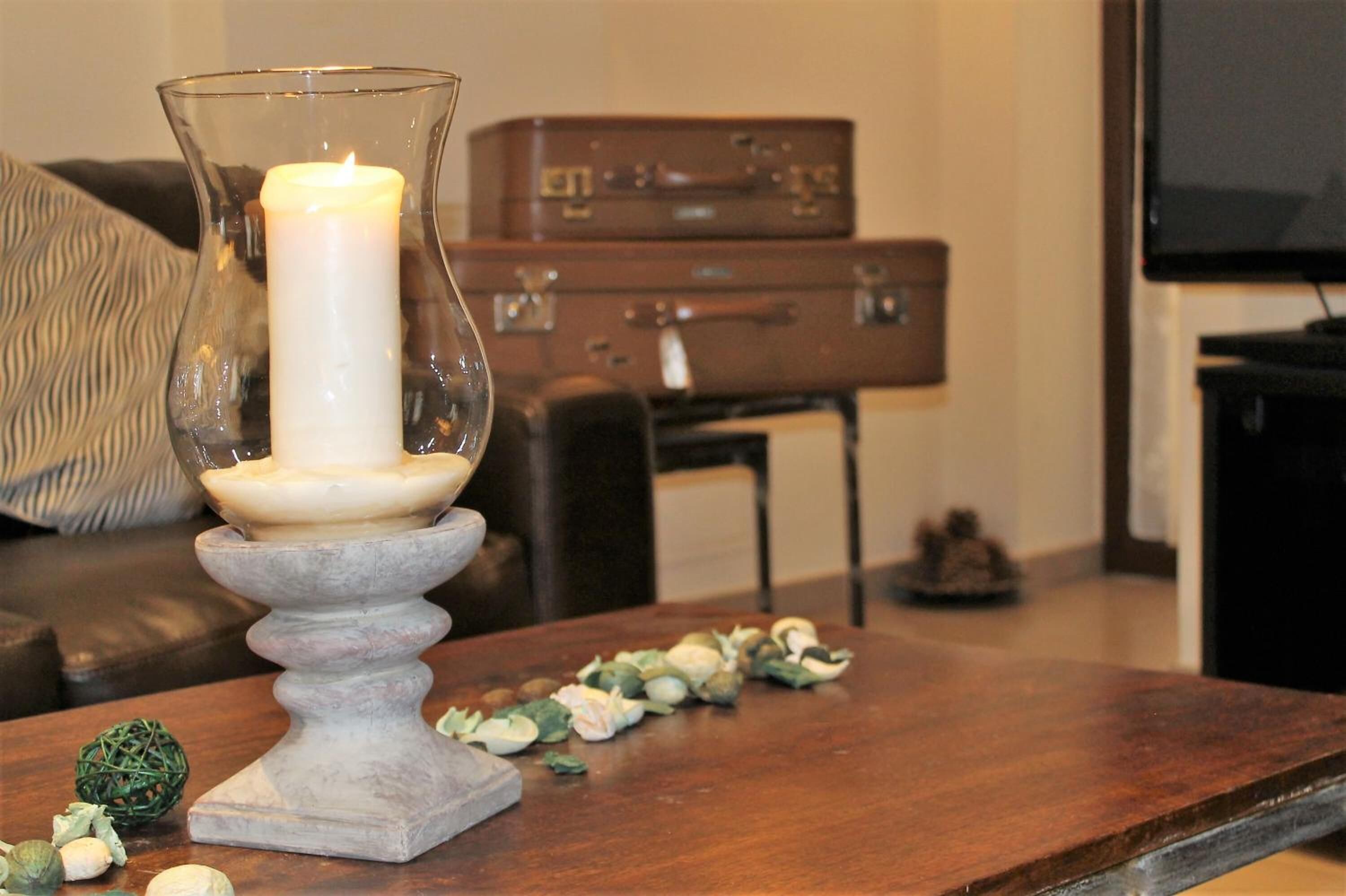 Una vela en un portavelas sobre una mesa de madera, rodeada de follaje verde.