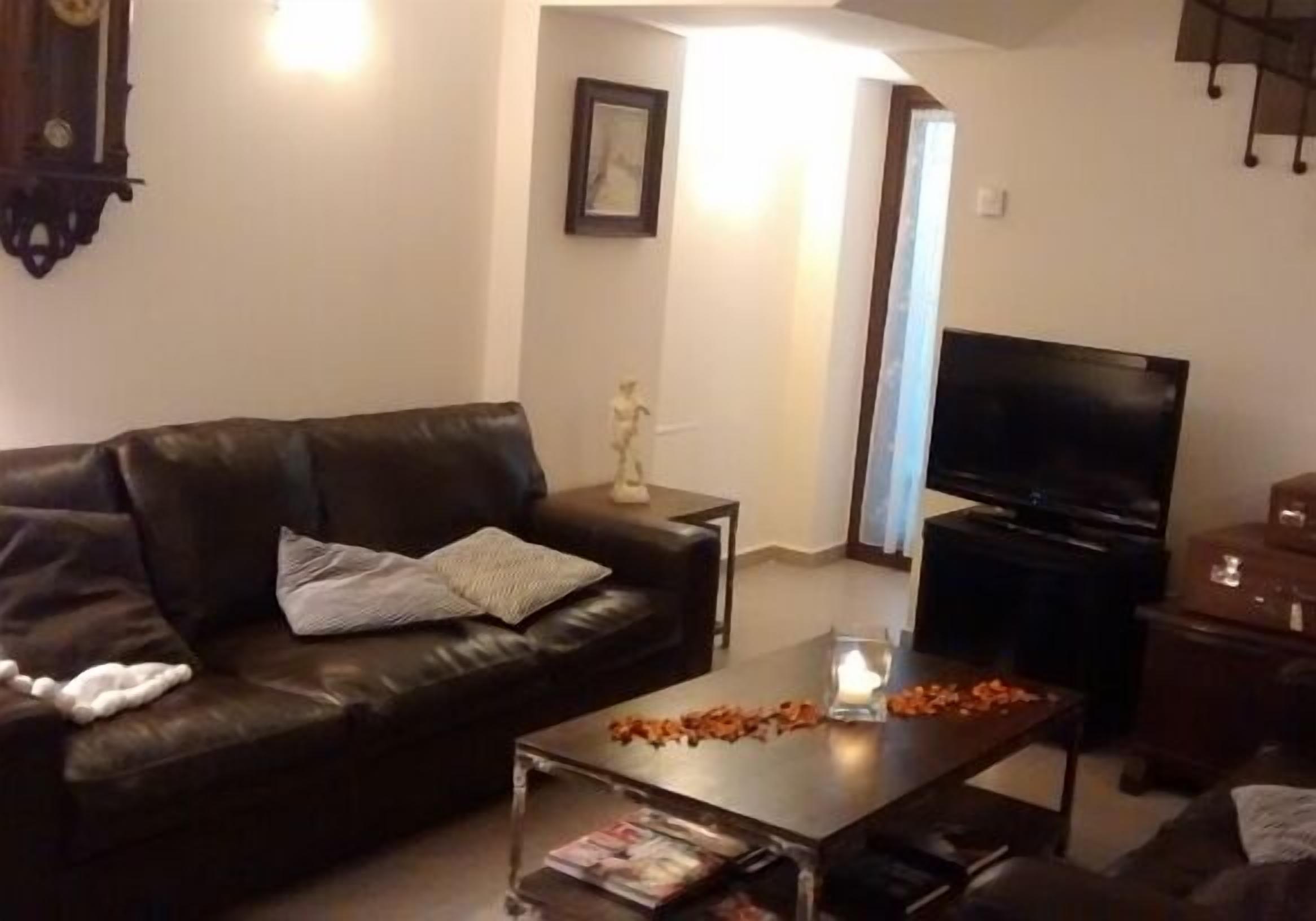 A living room with a leather sofa, a coffee table with magazines, a TV, and a fireplace.
