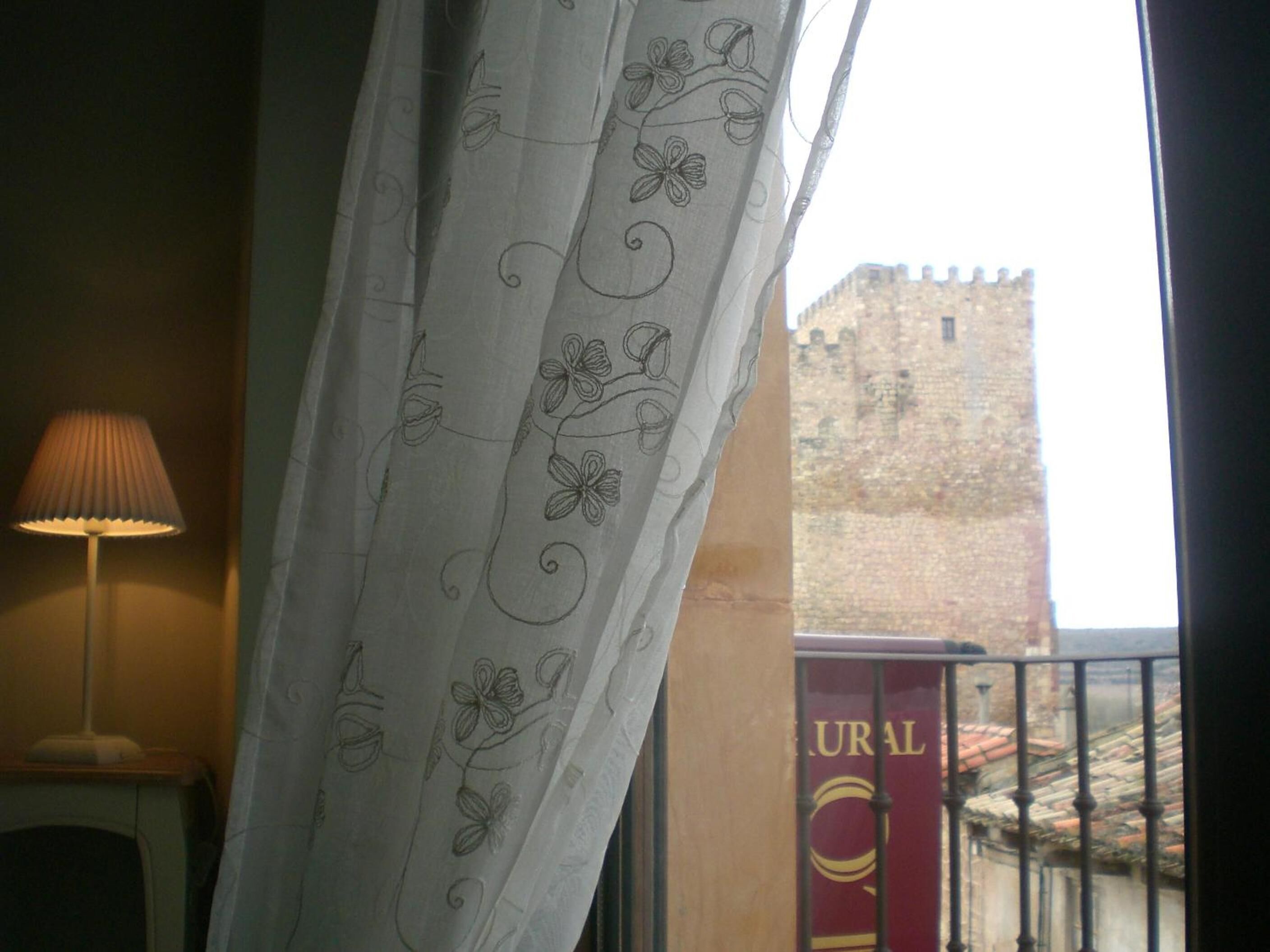 A room with a view of a castle through a window with a curtain featuring floral patterns.