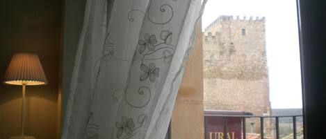 A room with a view of a castle through a window with a curtain featuring floral patterns.