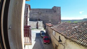 Eine enge Straße führt zu einer historischen Burg aus Stein mit einem Burggraben, geparkten Autos und traditionellen Ziegeldächern.