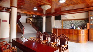 Vestíbulo de hotel con mostrador de recepción, sillas de madera, una escalera y una araña.