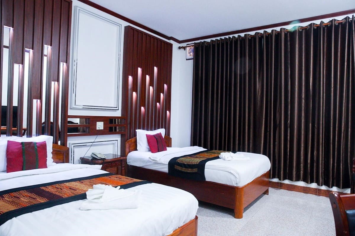 A hotel room with two beds, a desk, a telephone, and a window with dark curtains.
